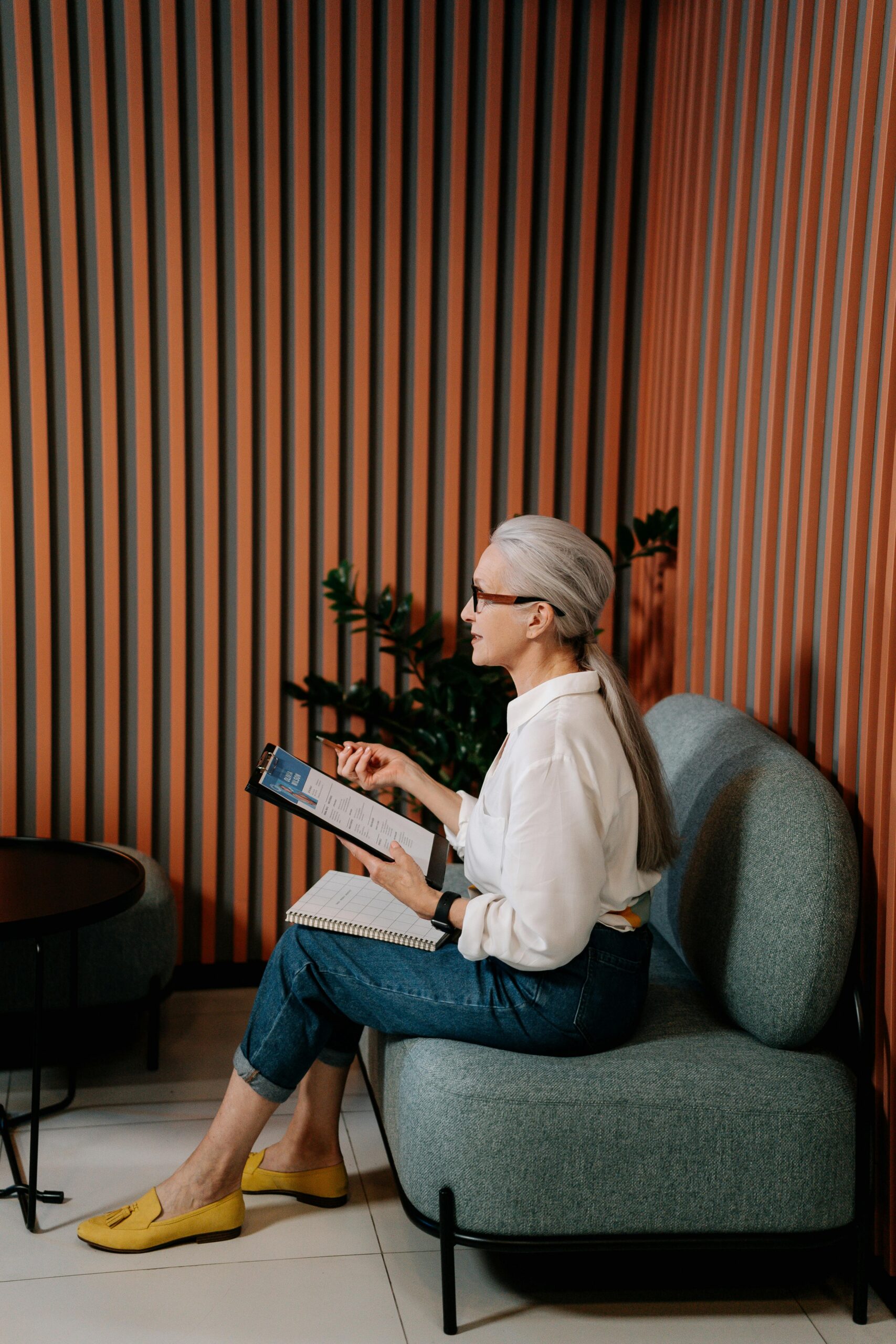 Woman in White Long Sleeve Shirt and Blue Denim Jeans Sitting on Gray Sofa Chair